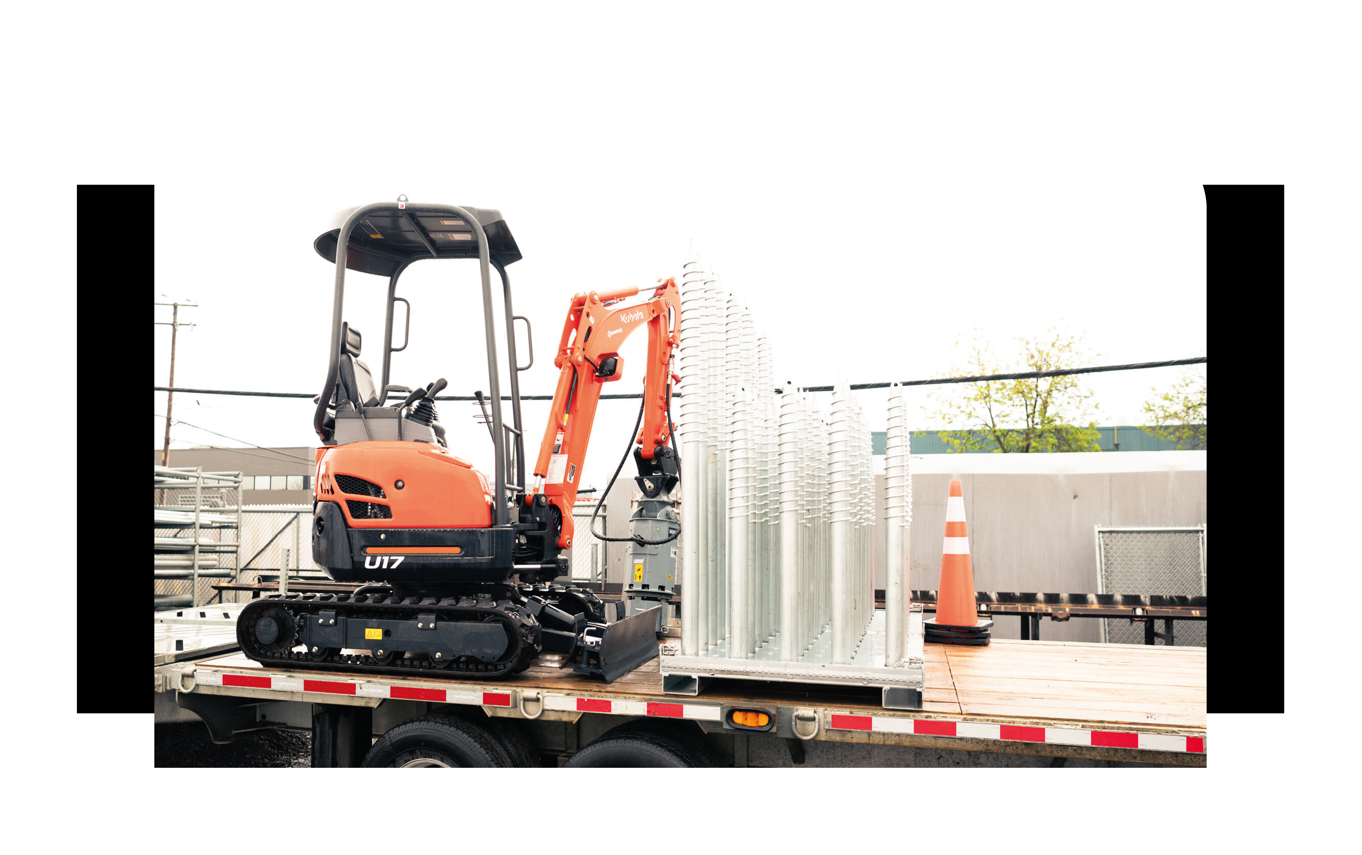 Mini-excavatrice et pieux galvanisés UPGRADE chargés sur un fardier, prêts pour le chantier