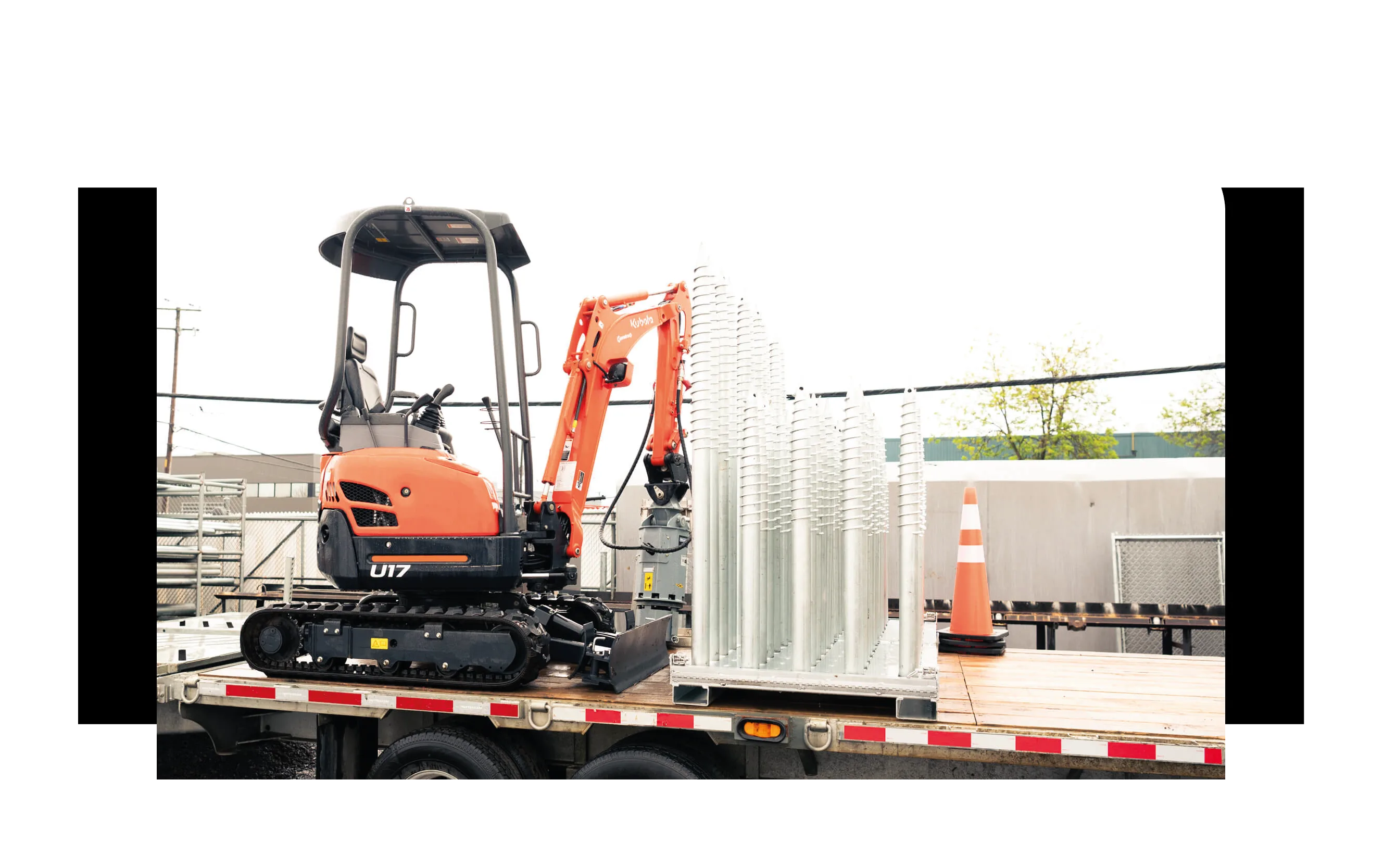Mini-excavatrice et pieux galvanisés UPGRADE chargés sur un fardier, prêts pour le chantier