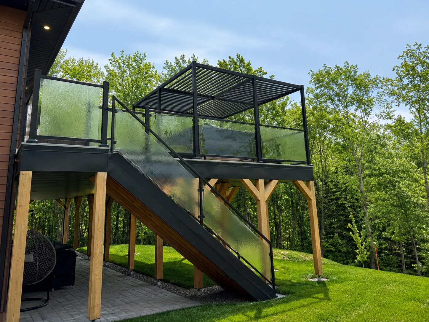 UPergolas noir sur terrasse surélevée sur pieux bois, vue escalier et garde-corps verre
